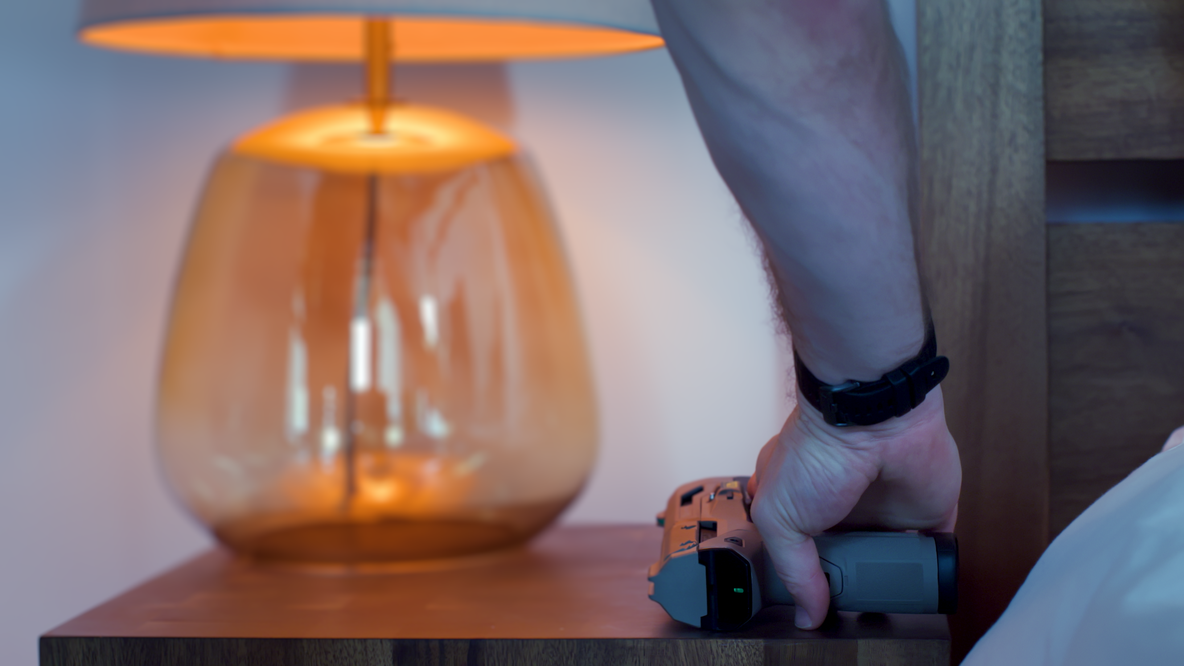 A hand picking up the Biofire Smart Gun beside a bedside lamp.