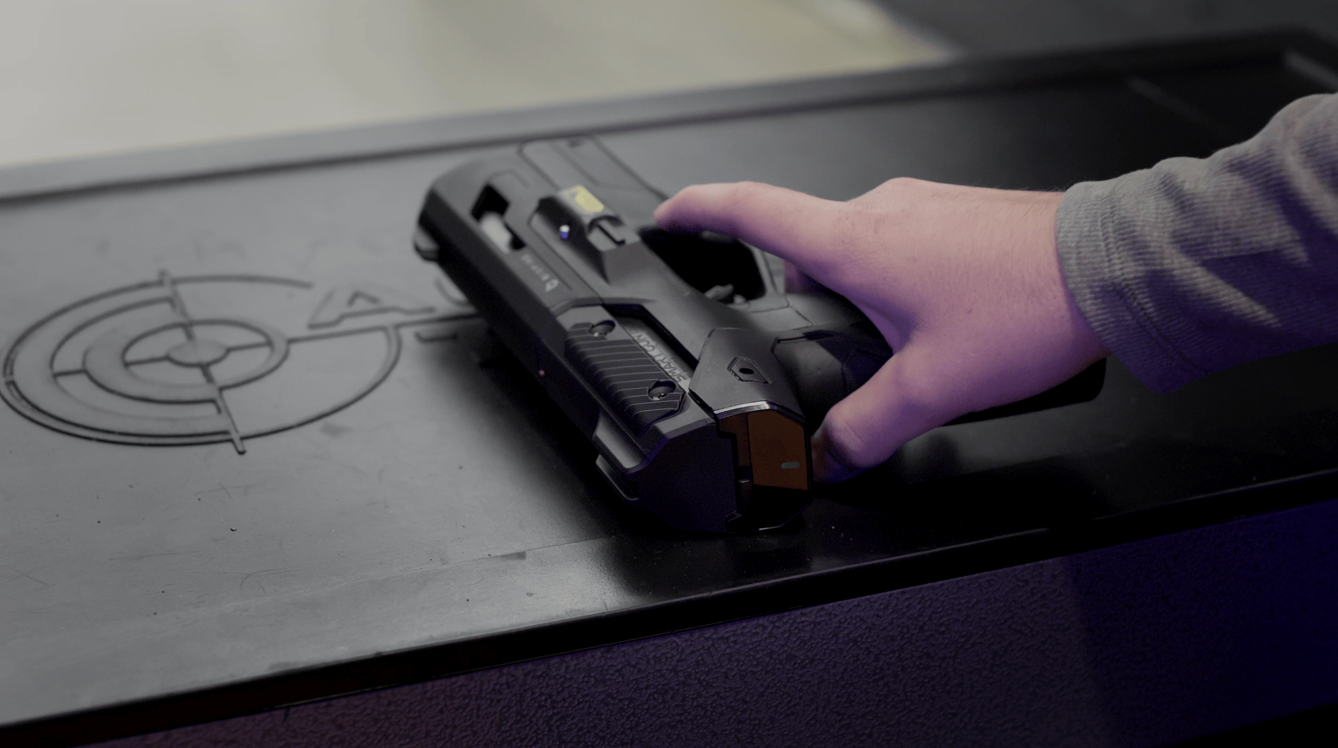 A hand picking up the Smart Gun from a dark tabletop.