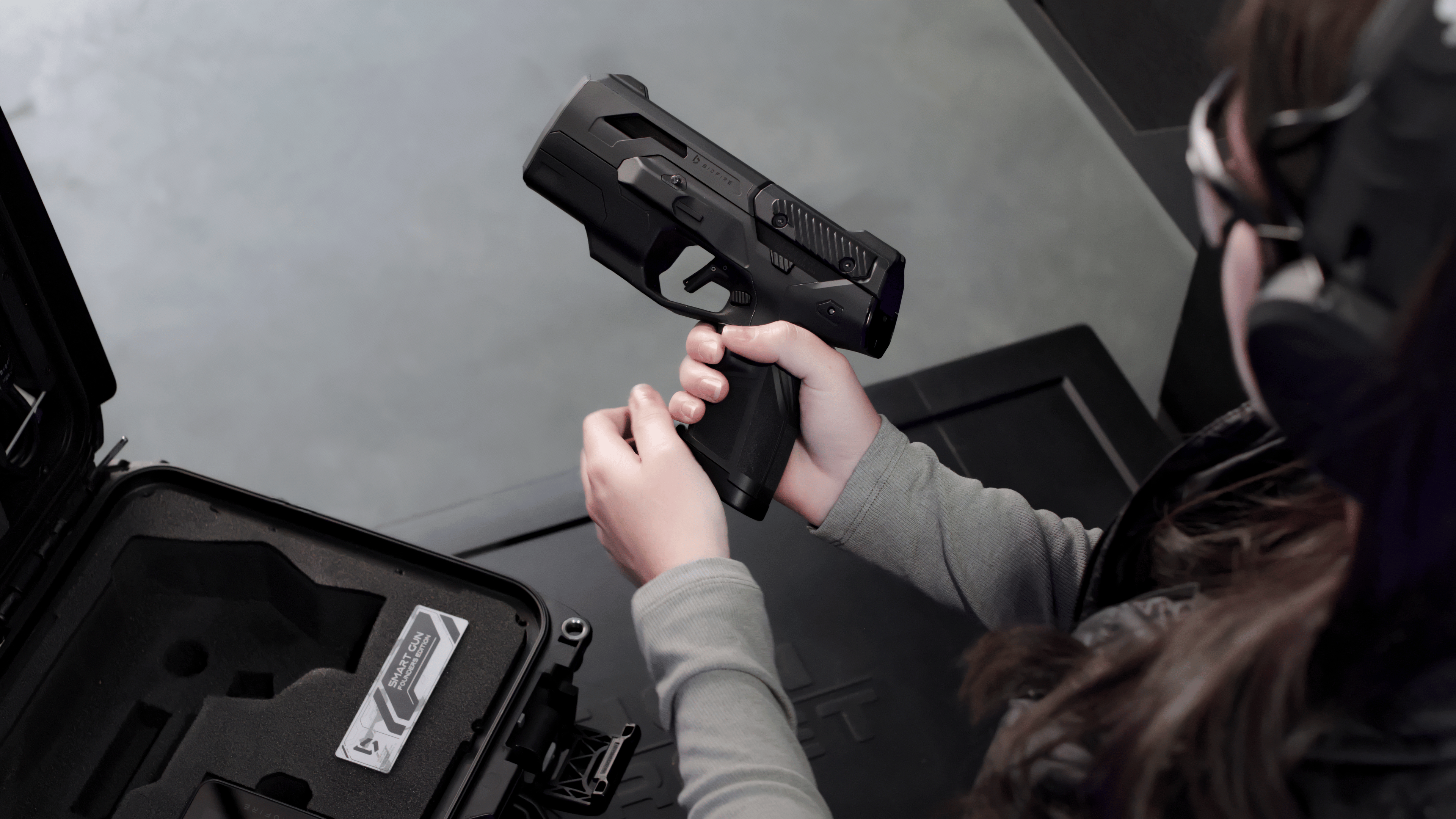 A woman handling the Smart Gun above its open case at an indoor range.