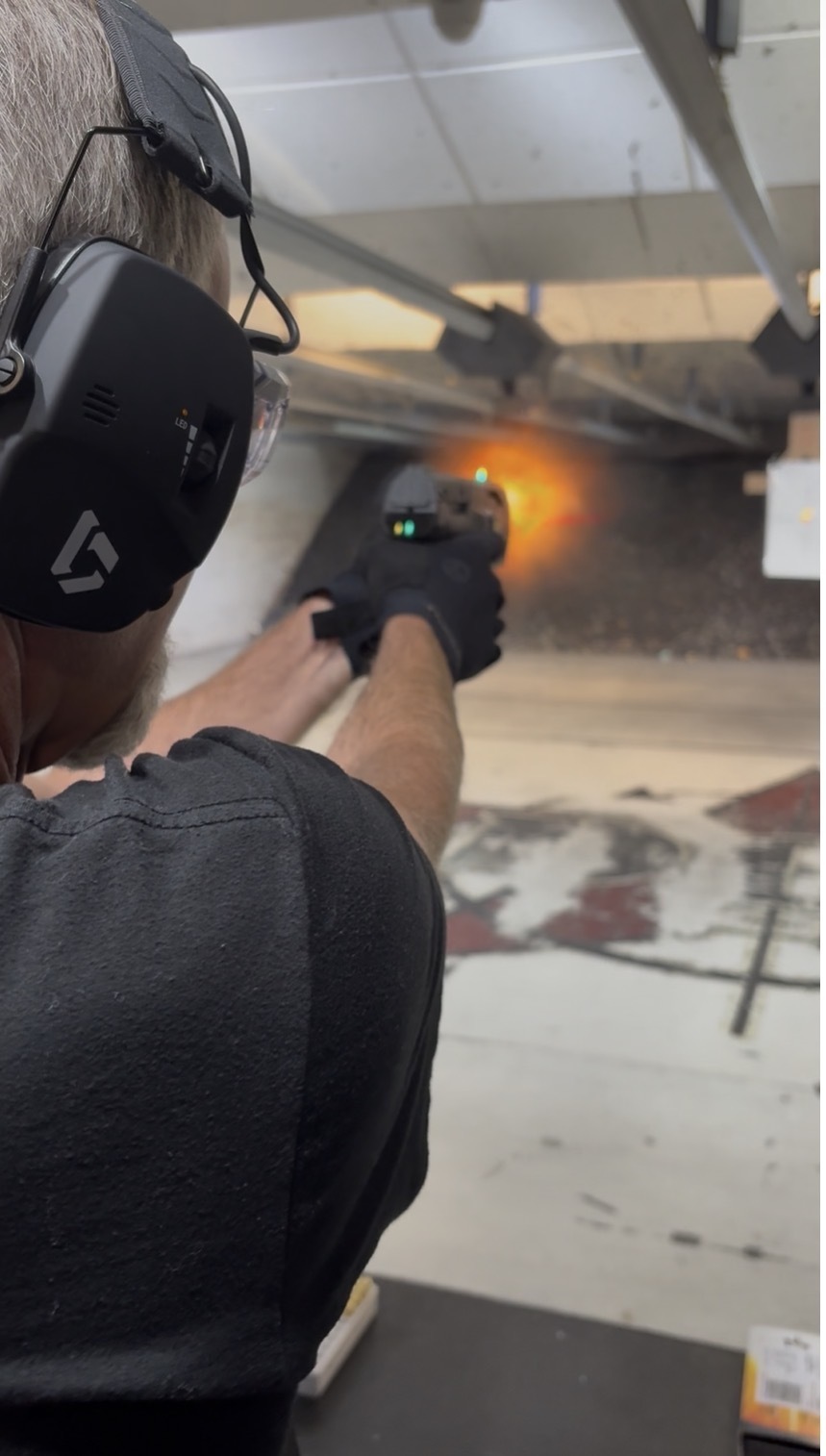 Ken firing the Smart Gun at an indoor range, with a muzzle flash visible.